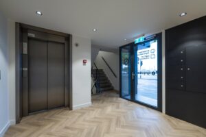 Moderne entreehal aan de Prins Hendrikkade met lift, trap en glazen toegangsdeur.